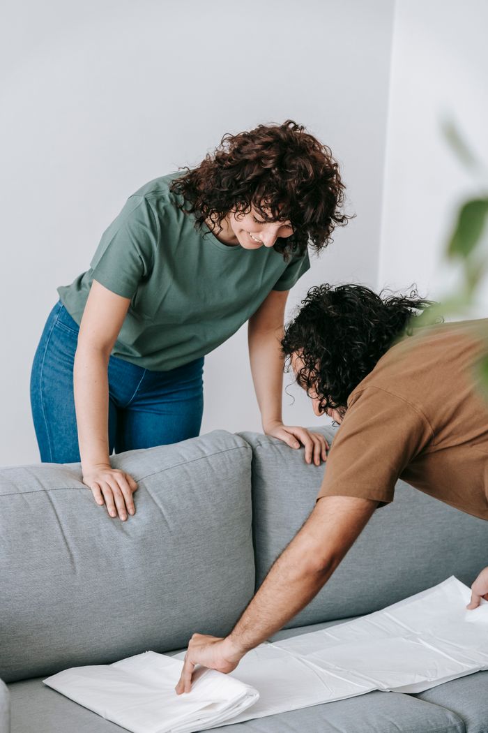 about-us-01 Couple preparing living room by covering the couch with protective white cloth.