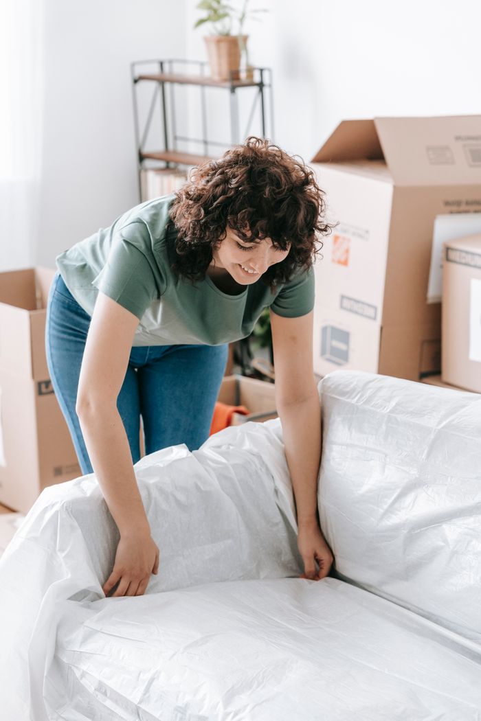 about-us-02 Woman wrapping a sofa with plastic for moving in a bright living room.